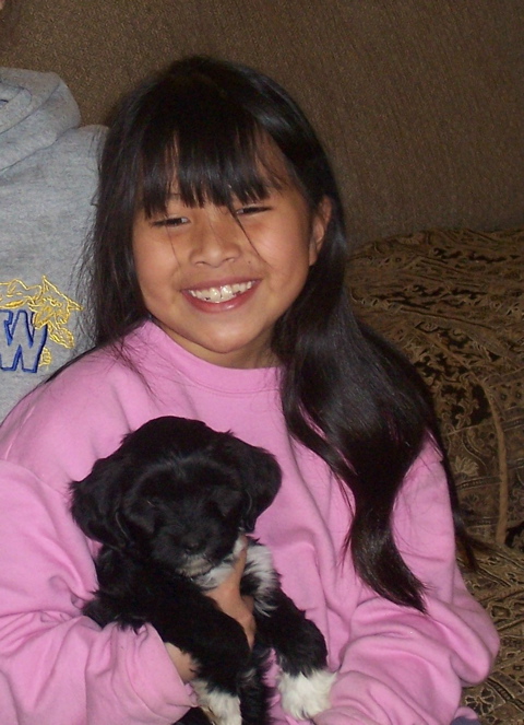 Girl in a pink top holding mostly black Tibetan Terrier