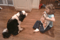 Young girl reading to a black-and-white Tibetan Terrier as both sit on a hardwood floor