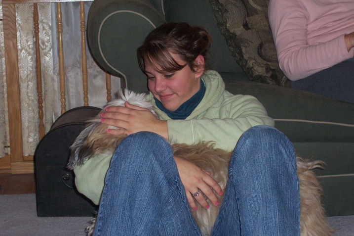 Young woman in green sweatshirt holding a sable Tibetan Terrier in her lap