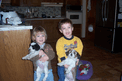Two small children, each holding a Tibetan Terrier puppy, one black and white, the other tan and white