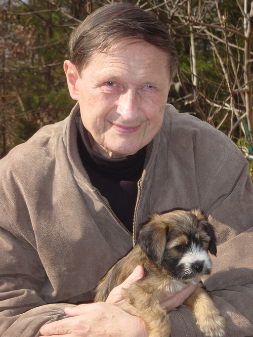 Man in tan fleece jacket holding small sable Tibetan Terrier puppy