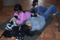 Two girls lying on a pad on a parquet floor with six young Tibetan Terrier puppies